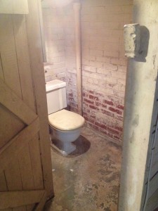 The original toilet behind the rough wooden partition.